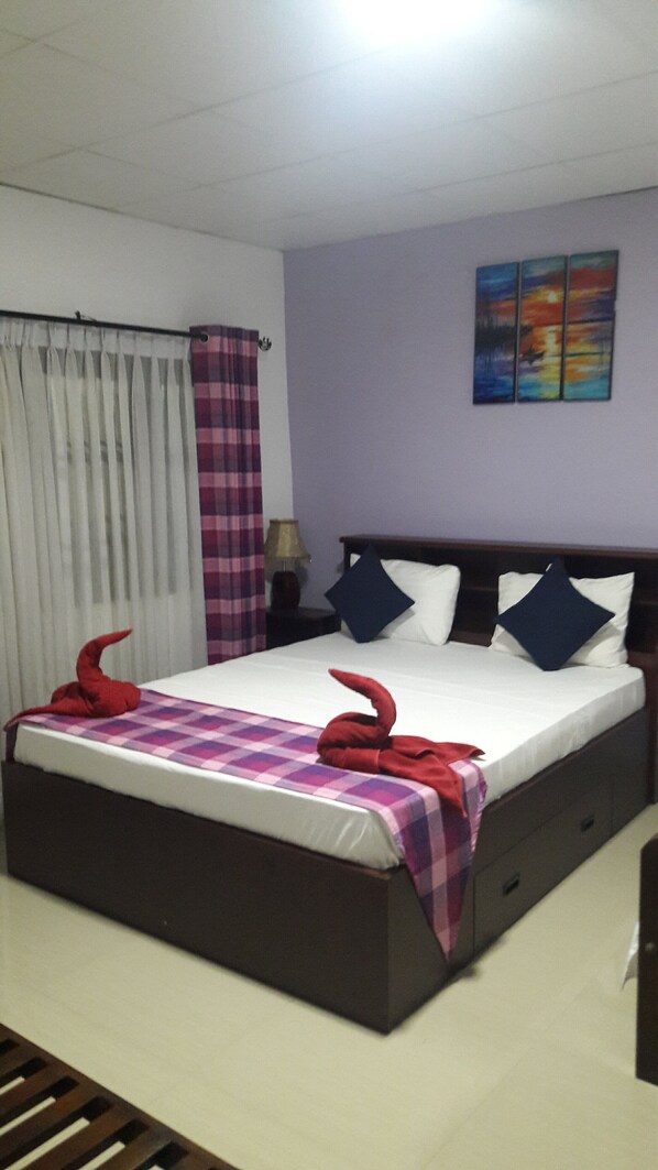 A hotel room with a large bed, a nightstand, a lamp, a painting on the wall, and a window with curtains.