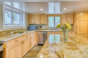 Una cocina con armarios de madera, encimeras de granito, lavavajillas y microondas.