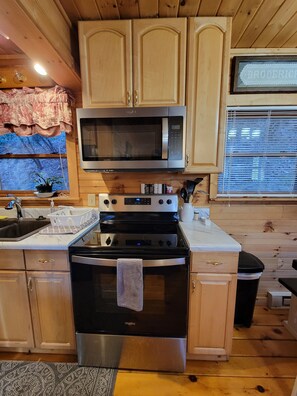 A kitchen with wooden cabinets, a stainless steel microwave, a stove, and a sink.