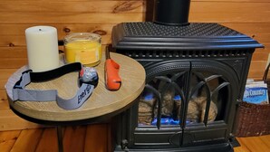 Een gezellige kamer met een houtkachel, een tafel met een kaars, een glas sinaasappelsap en een powerbank.