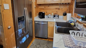 Een compacte keuken met houten kastjes, roestvrijstalen apparatuur en een aanrecht met koffiezetapparaat en broodrooster.