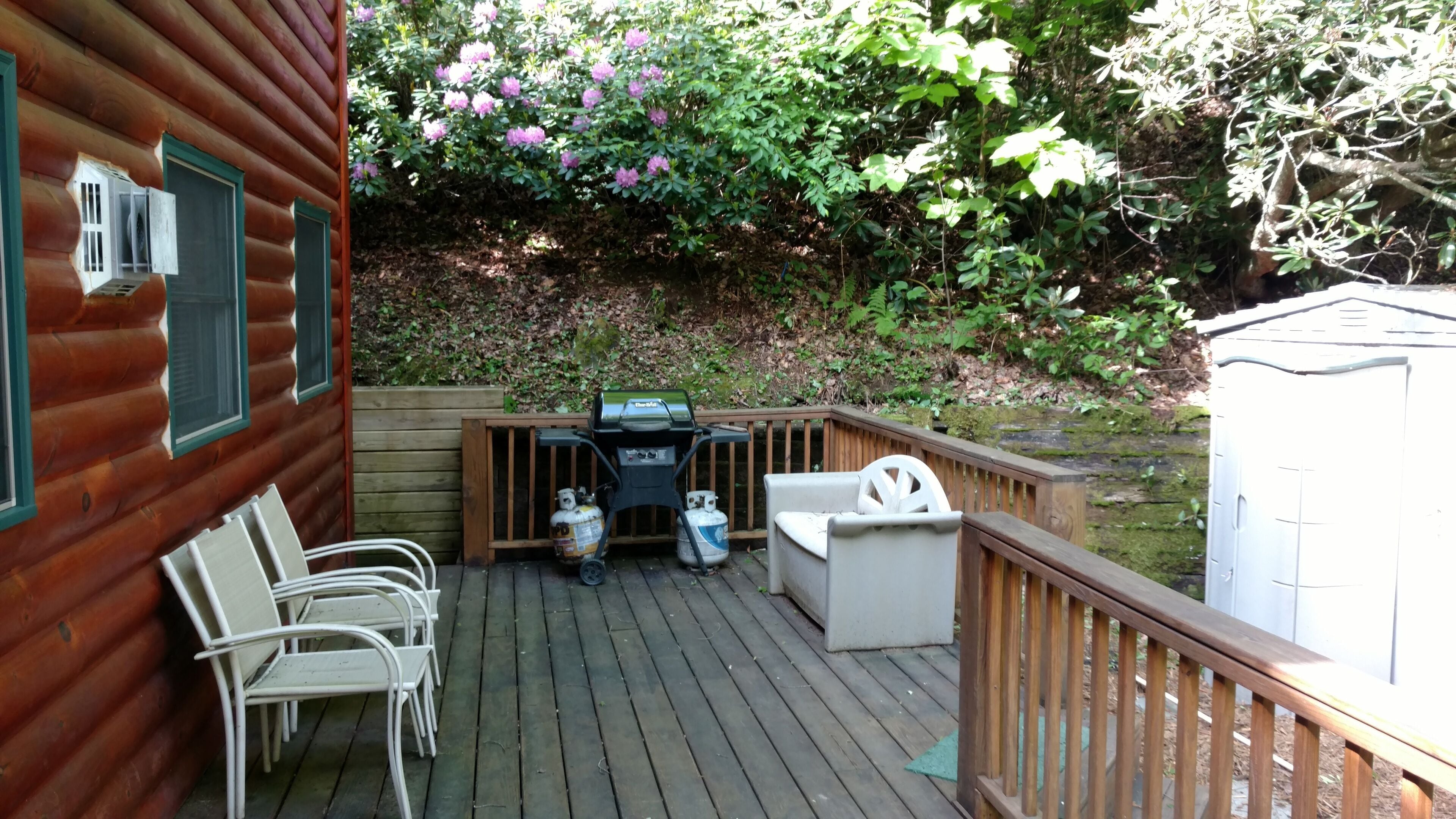 Een houten terras met buitenmeubilair, een barbecue en uitzicht op een tuin met bloeiende struiken.