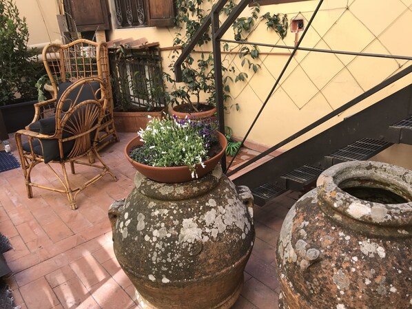A courtyard with terracotta pots, wicker furniture, and climbing plants.
