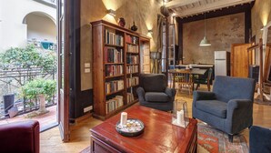 A cozy living room with a wooden bookshelf, a comfortable armchair, and a dining area visible through an open door. - Historical apartment in the heart of Florence with exclusive terrace (Firenze)