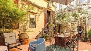 A patio area with a dining table, chairs, a blue chair, a glass table, and a staircase leading to an upper level. - Historical apartment in the heart of Florence with exclusive terrace (Firenze)