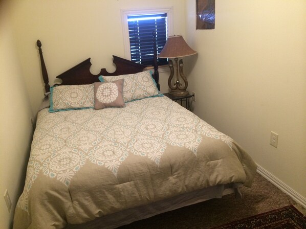 A bedroom with a bed, a window with blinds, a lamp, and a carpeted floor.