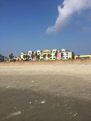 Un hotel frente a la playa con varios edificios de colores, una playa arenosa y un cielo azul despejado.