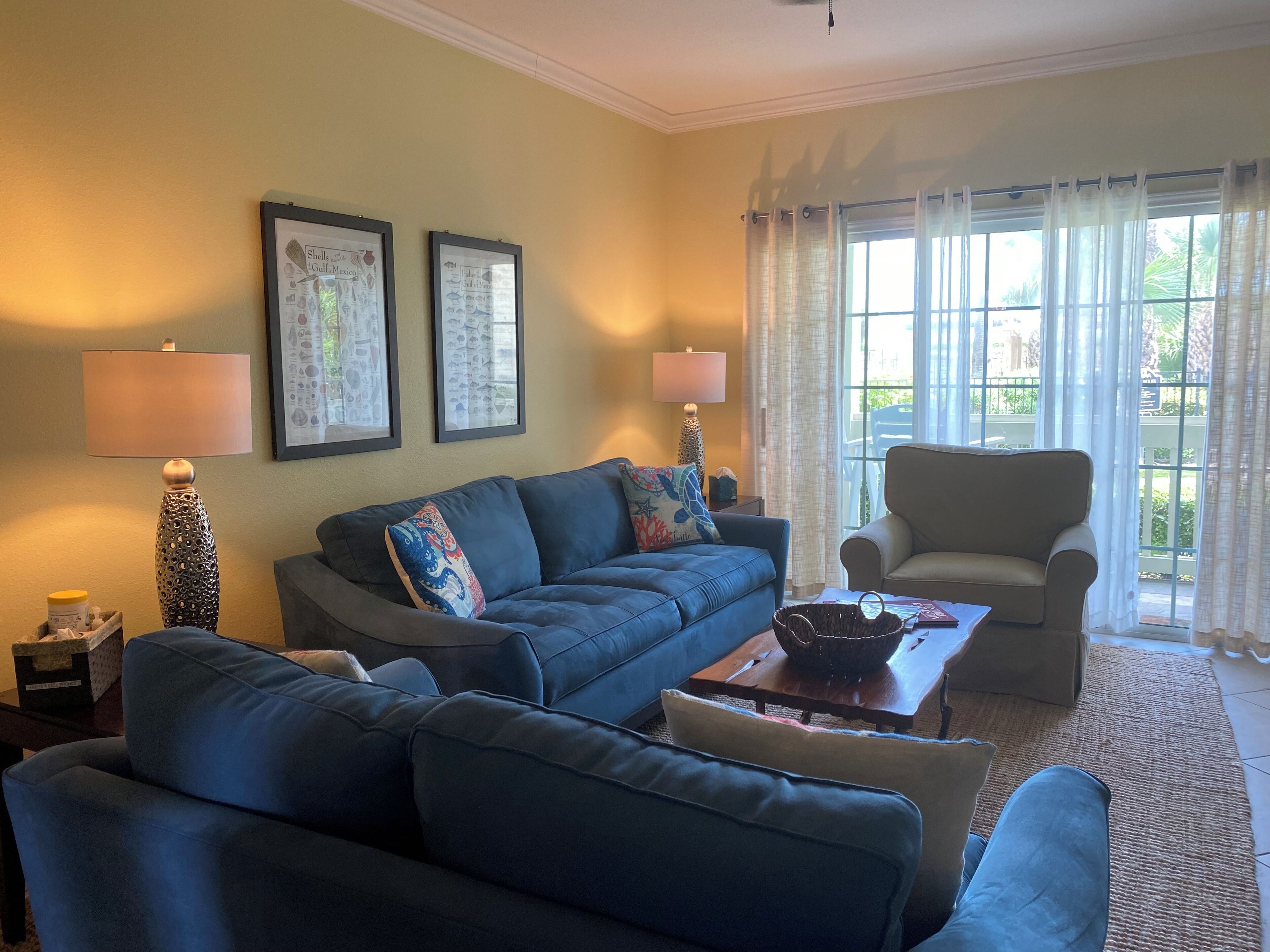 Una sala de estar con un sofá azul, un sillón beige, dos lámparas y una ventana con cortinas.