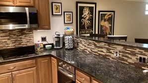 A modern kitchen with wooden cabinets, a stainless steel microwave, a coffee maker, and a tiled backsplash.