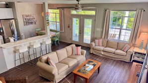 A spacious living room with a beige sofa, a wooden coffee table, and a kitchen area with a refrigerator and bar stools.
