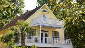 A yellow house with a balcony, surrounded by greenery.