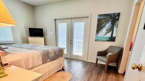 A bedroom with a bed, a desk, a chair, a TV, and a balcony with a view.