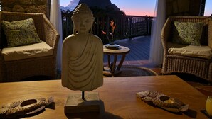 Un espace extérieur paisible, aménagé avec des meubles en osier et agrémenté d’une statue de Bouddha, offrant une vue imprenable sur un paysage montagneux.