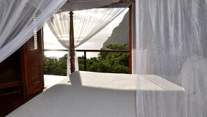 Un balcon avec un lit, des rideaux blancs et une vue sur une falaise et des arbres.