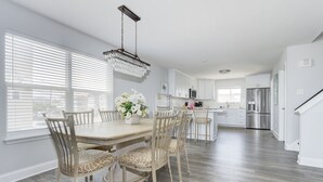 A modern kitchen with white cabinets, stainless steel appliances, and a dining area with a wooden table and chairs. - Oceanfront! Fenced in back yard! Pet Friendly! Come visit anytime👍 (Brigantine)