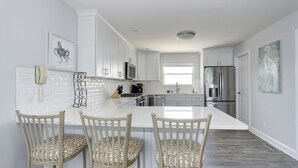 A modern kitchen with white cabinetry, a large island with bar stools, and stainless steel appliances. - Oceanfront! Fenced in back yard! Pet Friendly! Come visit anytime👍 (Brigantine)