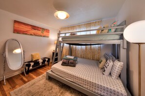 A bunk bed with a patterned bedspread, a mirror, a cow print bench, and a painting on the wall.