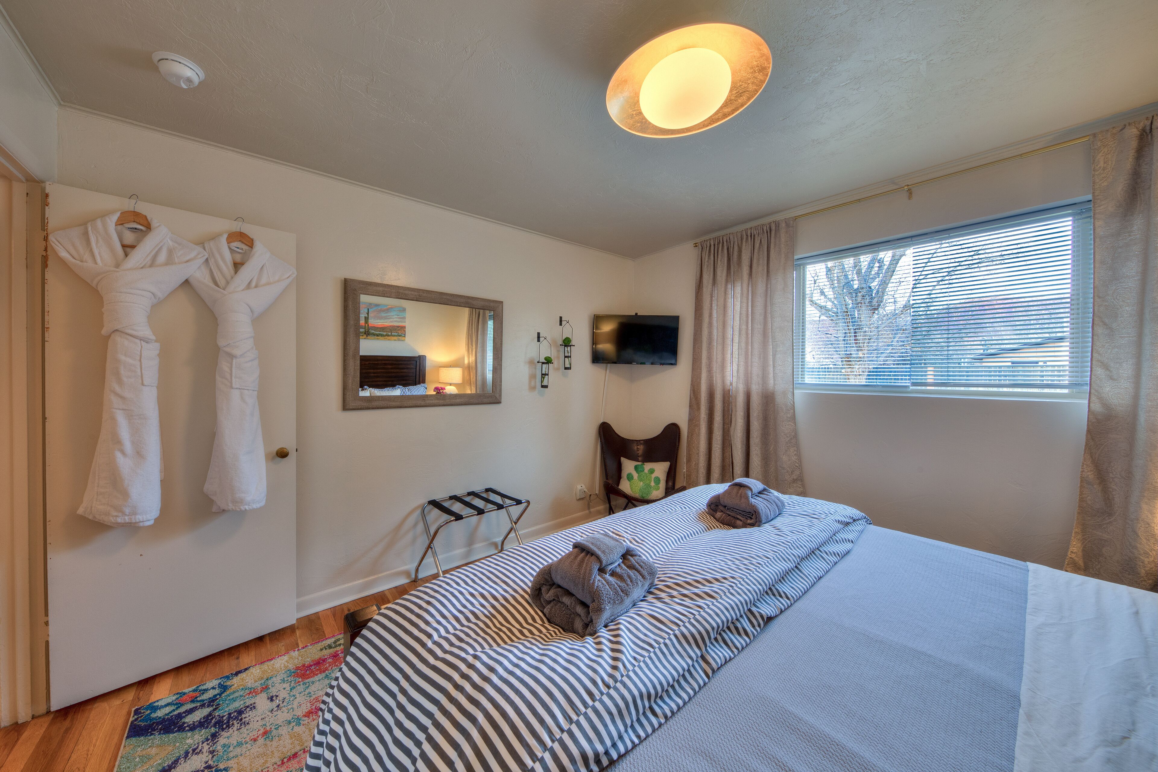 Une chambre d’hôtel avec un lit, une télévision, une fenêtre avec des rideaux et deux serviettes accrochées au mur.