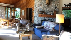 A cozy cabin interior with a stone fireplace, wooden ceiling, and a dining area with a table and chairs.