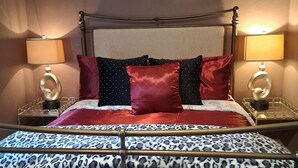 Una cama con estructura metálica, dos lámparas de noche y una colcha estampada.