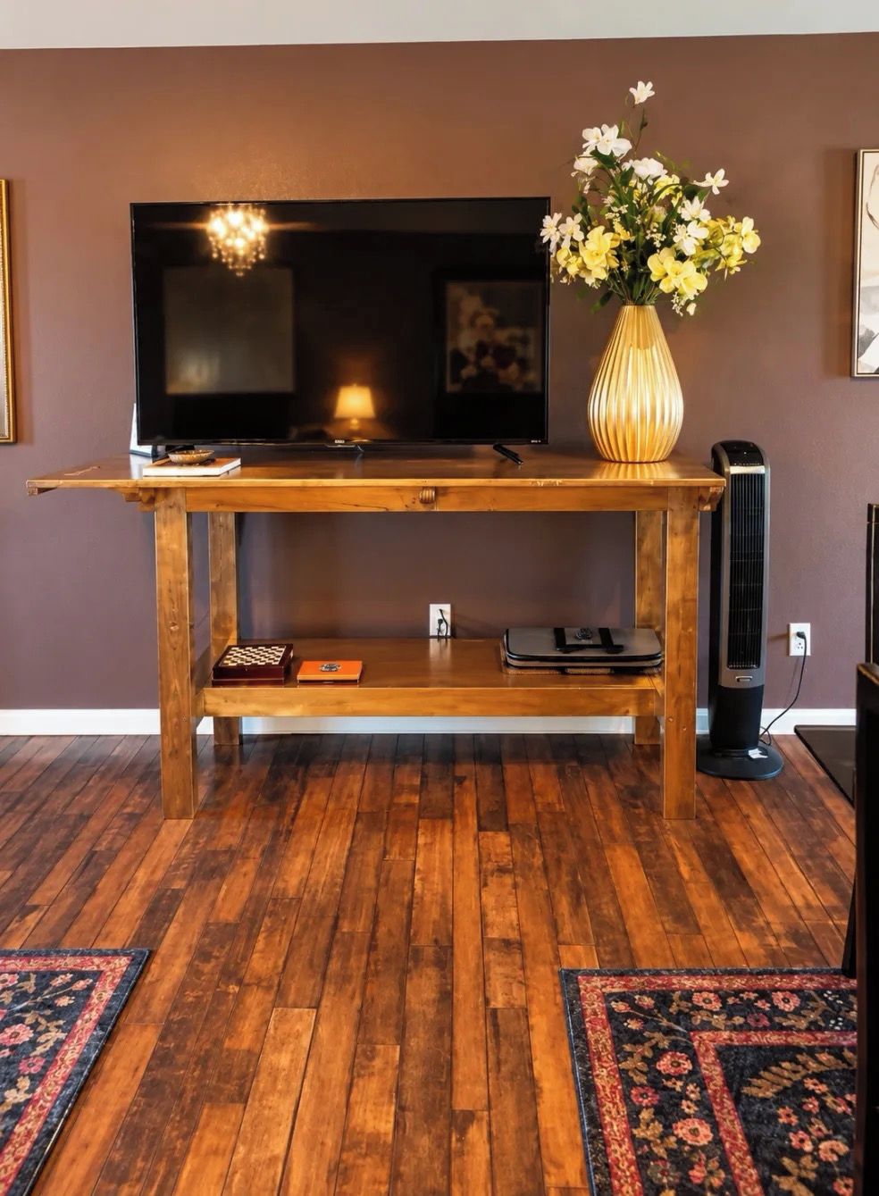 A wooden entertainment center with a flat-screen TV, a vase with flowers, and a standing fan.