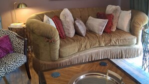 Un salon avec un canapé beige, un fauteuil à motifs, une table basse ronde et un lampadaire.