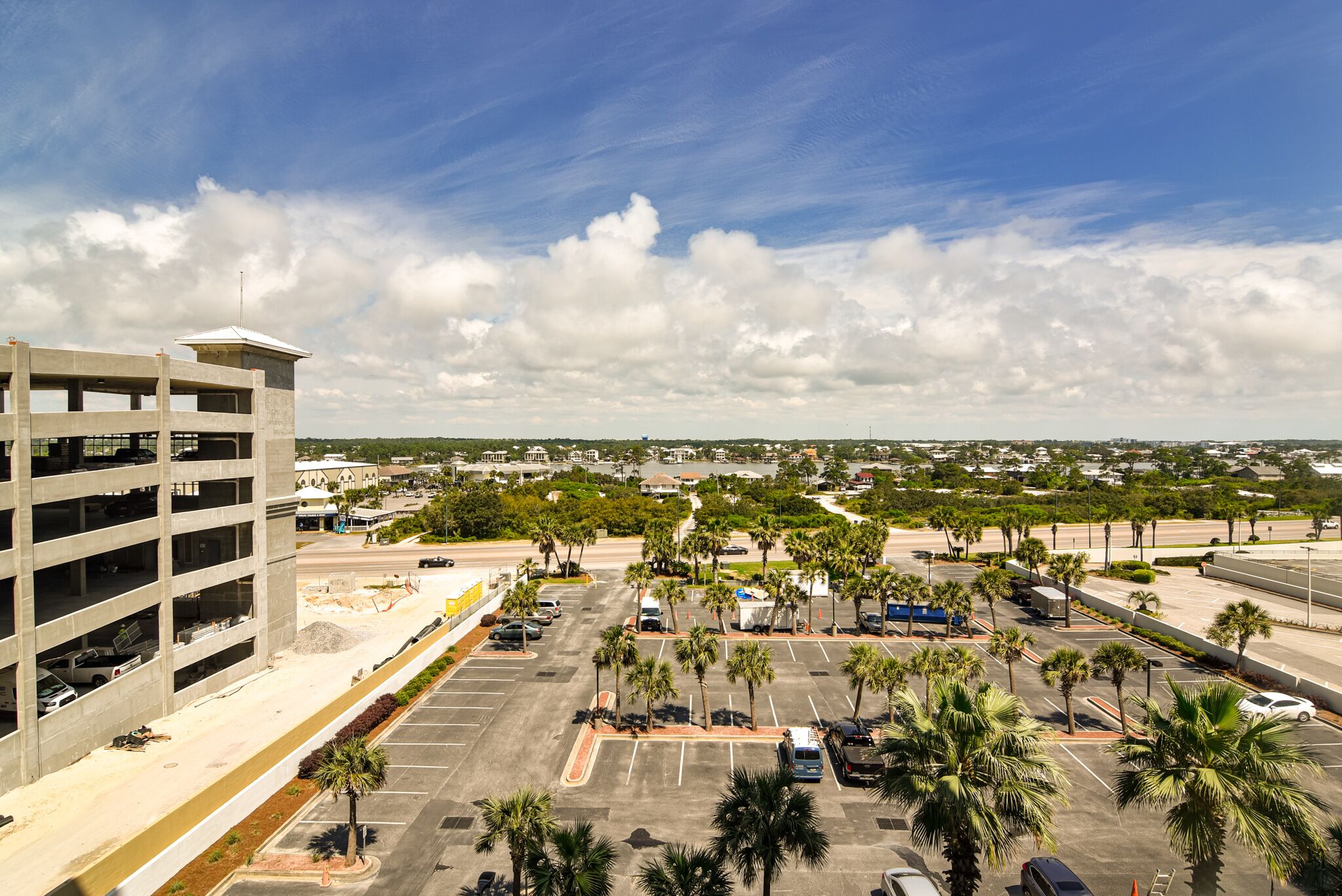 A parking lot with multiple rows of parking spaces, a multi-story parking garage, and palm trees.