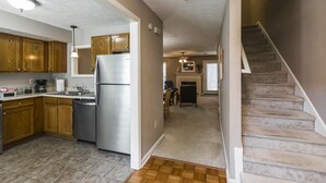 A kitchen with wooden cabinets, a stainless steel refrigerator, and a dining area with a fireplace. - 3 Bedroom Downtown Townhouse, Close to All!  (Lexington)