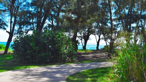 A paved pathway curving through a park with trees and a view of the ocean. - Very,  very affordable. Steps to paved, oceanfront path. Oceanside, end unit (Kapaa)