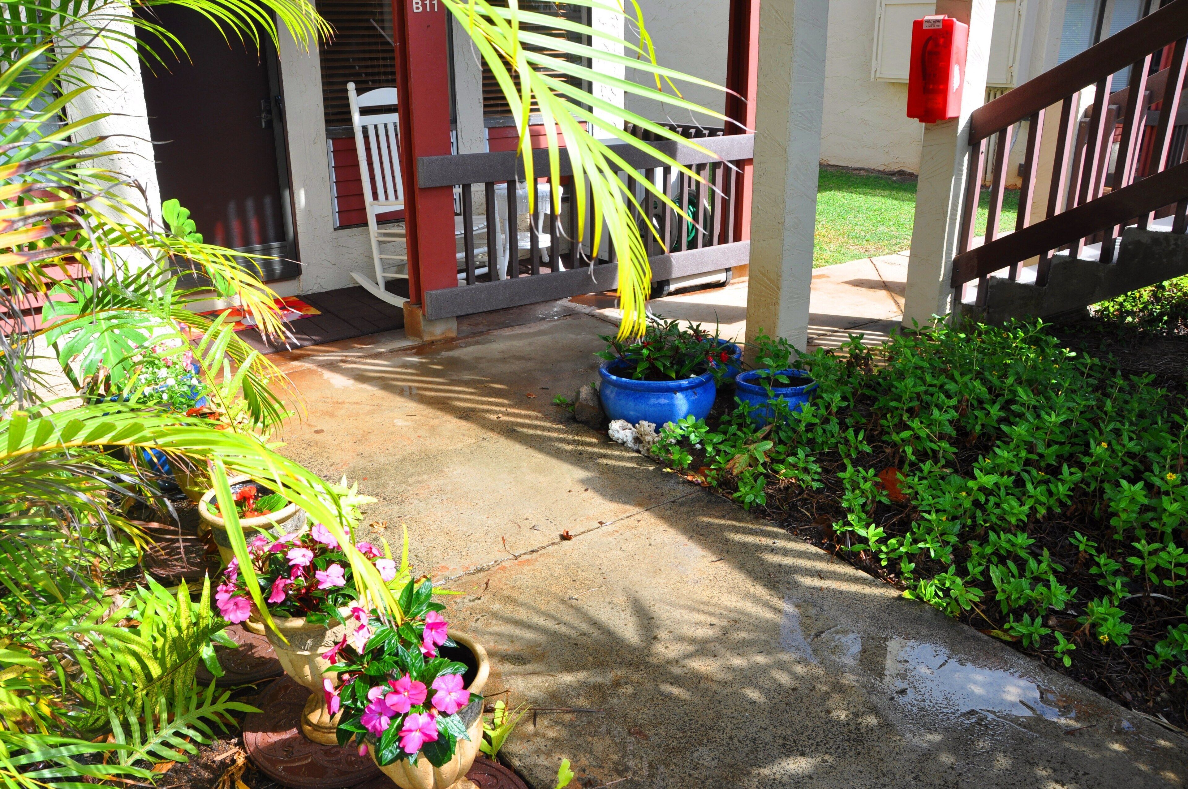 A concrete pathway leading to a building entrance with a wooden porch and a red mailbox.