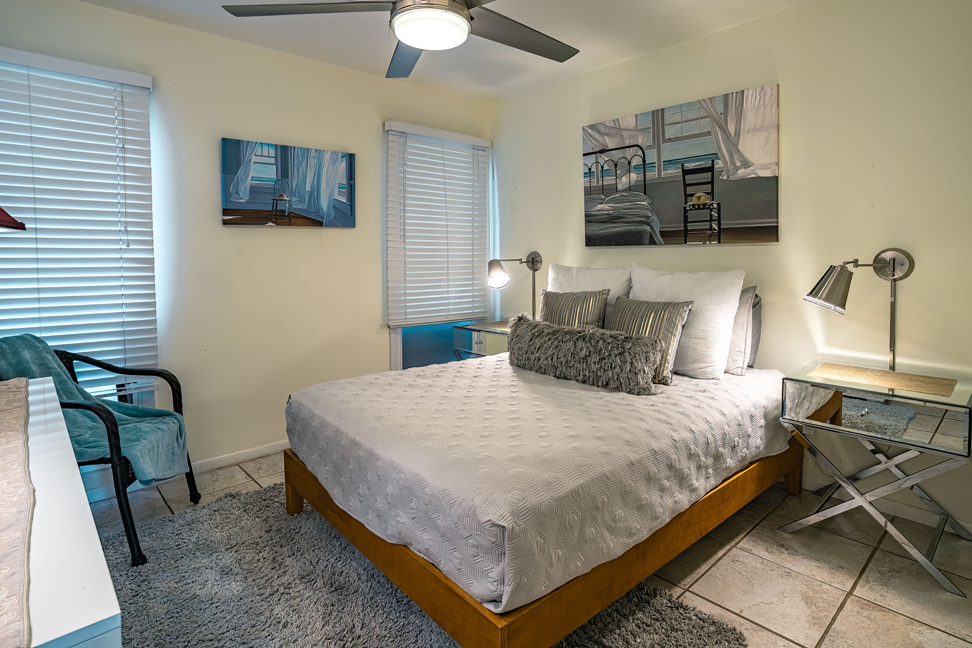 A bedroom with a bed, two bedside tables, a desk, a chair, and artwork on the walls.