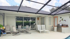 A covered outdoor area with a pool, lounge chairs, a table, and a grill. - Kid Friendly Home W/Pool  in Gated Community,10 Min. to Disney (Kissimmee)