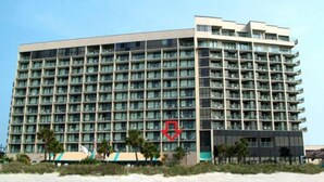 Un hotel de varios pisos con un diseño arquitectónico moderno, que cuenta con numerosos balcones y un amplio frente de cristal.