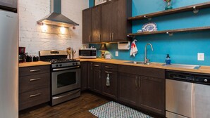 A modern kitchen with dark wooden cabinets, stainless steel appliances, a brick wall, and blue accents. - Artistic Loft close to Lake Michigan beaches, craft breweries & outlet shopping (Michigan City)