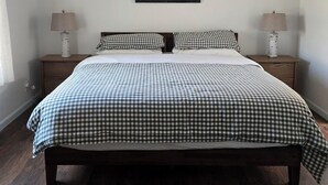 A bedroom with a large bed, two bedside tables with lamps, a wall-mounted picture, and wooden flooring.