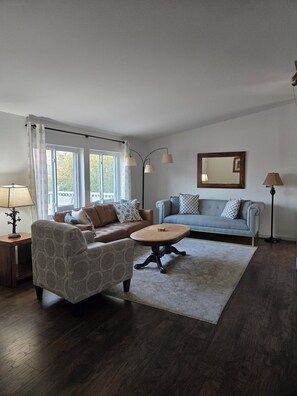A living room with a brown sofa, a patterned armchair, a round coffee table, and a floor lamp. - Hillside at Emigrant Creek Ranch (Ashland)