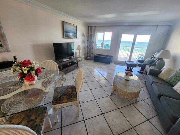 A living room with a TV, wicker furniture, a glass coffee table, and a view of the ocean. - Beach front Condo with gorgeous views of the Gulf and 300 Feet of Private Beach (Destin)