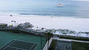 A beach with a tennis court, a lifeguard tower, and a boat in the water.