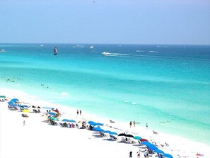 A beach with white sand and clear turquoise water. There are several umbrellas and people on the beach. - Beach front Condo with gorgeous views of the Gulf and 300 Feet of Private Beach (Destin)