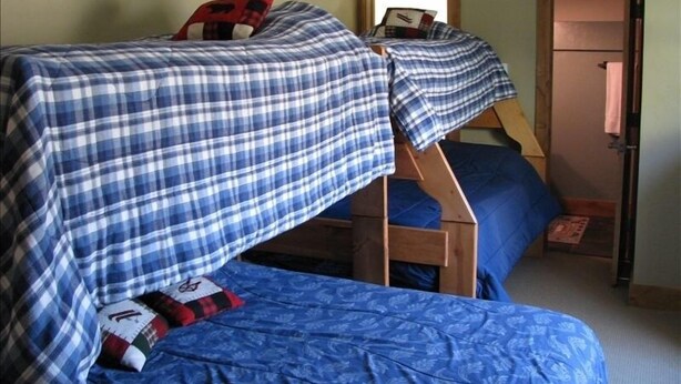 A room with two bunk beds, each with a blue and white checkered blanket and a pillow with a red and black design. - 3 Bedroom Condo,  Great Location for Ski Families to Super Bee Lift (Copper Mountain)