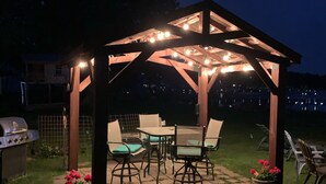 A covered outdoor seating area with string lights, a grill, and potted plants.