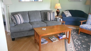 A living room with a grey sofa, a blue sofa, a wooden coffee table, and a small side table with a lamp.