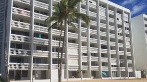 Un hôtel à plusieurs étages doté de balcons, d’un palmier et d’une plage de sable au premier plan.