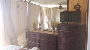Une chambre d’hôtel avec un lit, un téléviseur posé sur un meuble, un ventilateur de plafond, un miroir et une fenêtre avec des rideaux.
