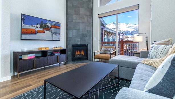 A modern living room with a fireplace, a sofa, a coffee table, and a large window offering a view of a snowy landscape. - Ski In/Out 2BD Top floor W/Amazing Views (Park City)