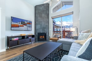 Uma sala de estar moderna com lareira, um sofá, uma mesa de centro e uma janela ampla com vista para uma paisagem nevada.