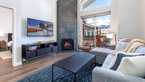 A modern living room with a fireplace, comfortable seating, and a large window offering a view of the outdoors. - Ski In/Out 2BD Top floor W/Amazing Views (Park City)