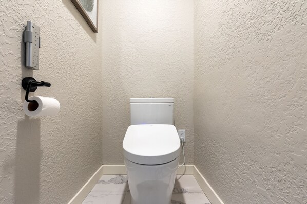 Une petite salle de bain équipée de toilettes, d’un distributeur d’essuie-tout et d’une prise électrique murale.