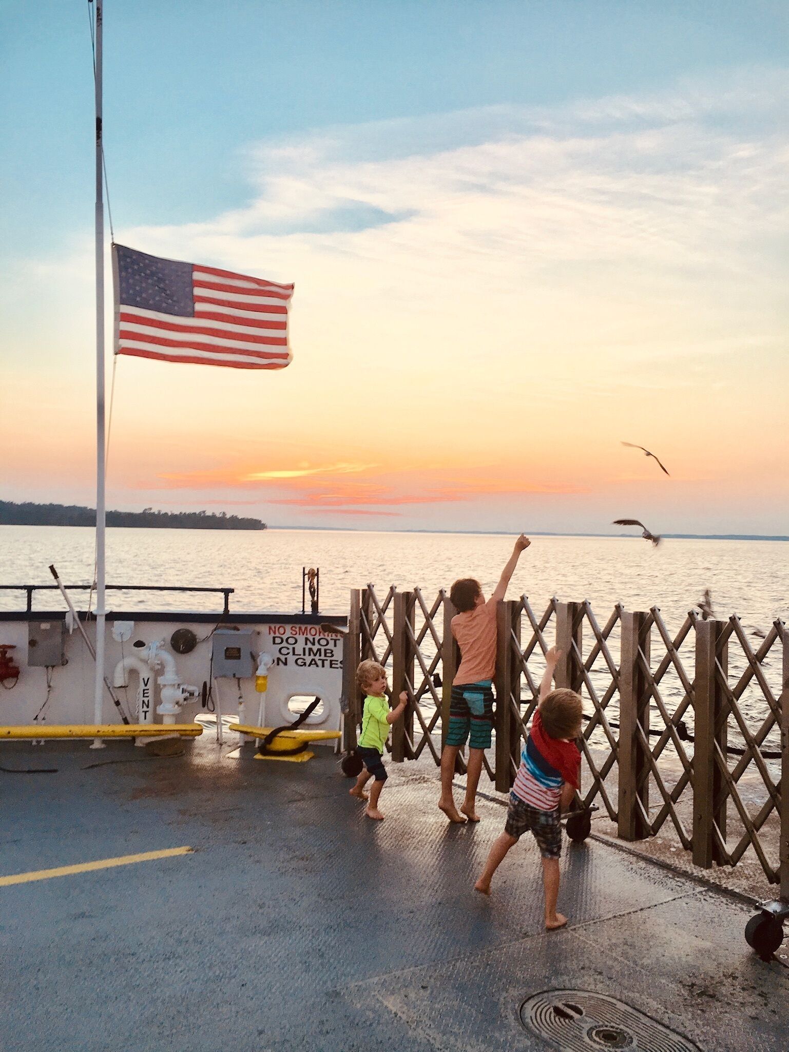 Une vue sur le coucher de soleil depuis une jetée, avec un drapeau américain, un panneau interdisant de fumer et une rambarde.