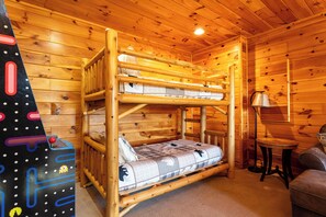 Uma cama de beliche em um quarto de cabana de madeira, com uma mesa pequena e um abajur.